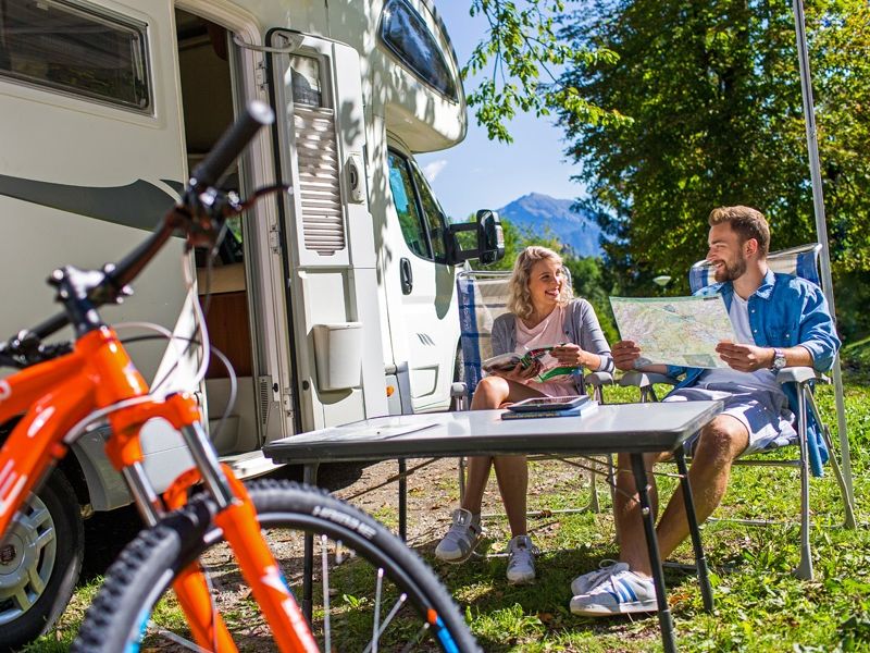 Twee mensen zitten voor camper met tafel en mountainbike