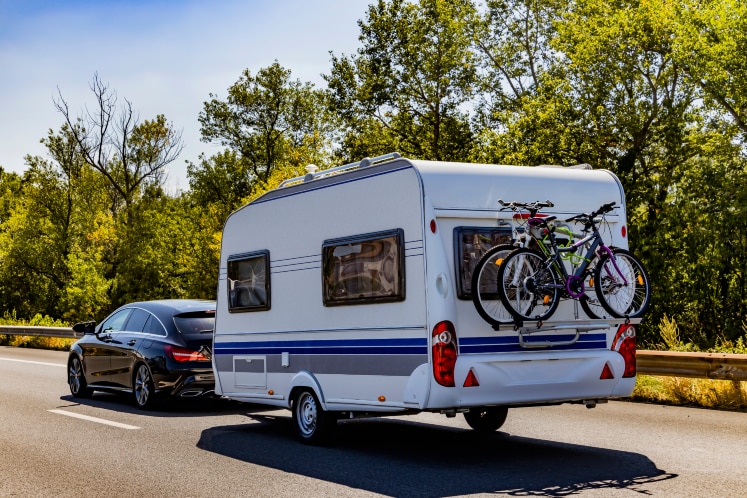 Auto rijdt met caravan en fietsen achterop