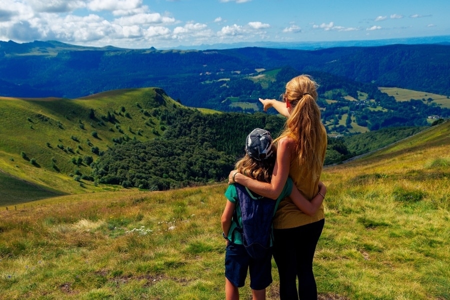 moeder en zoon kijken uit over een groen, heuvelachtig landschap