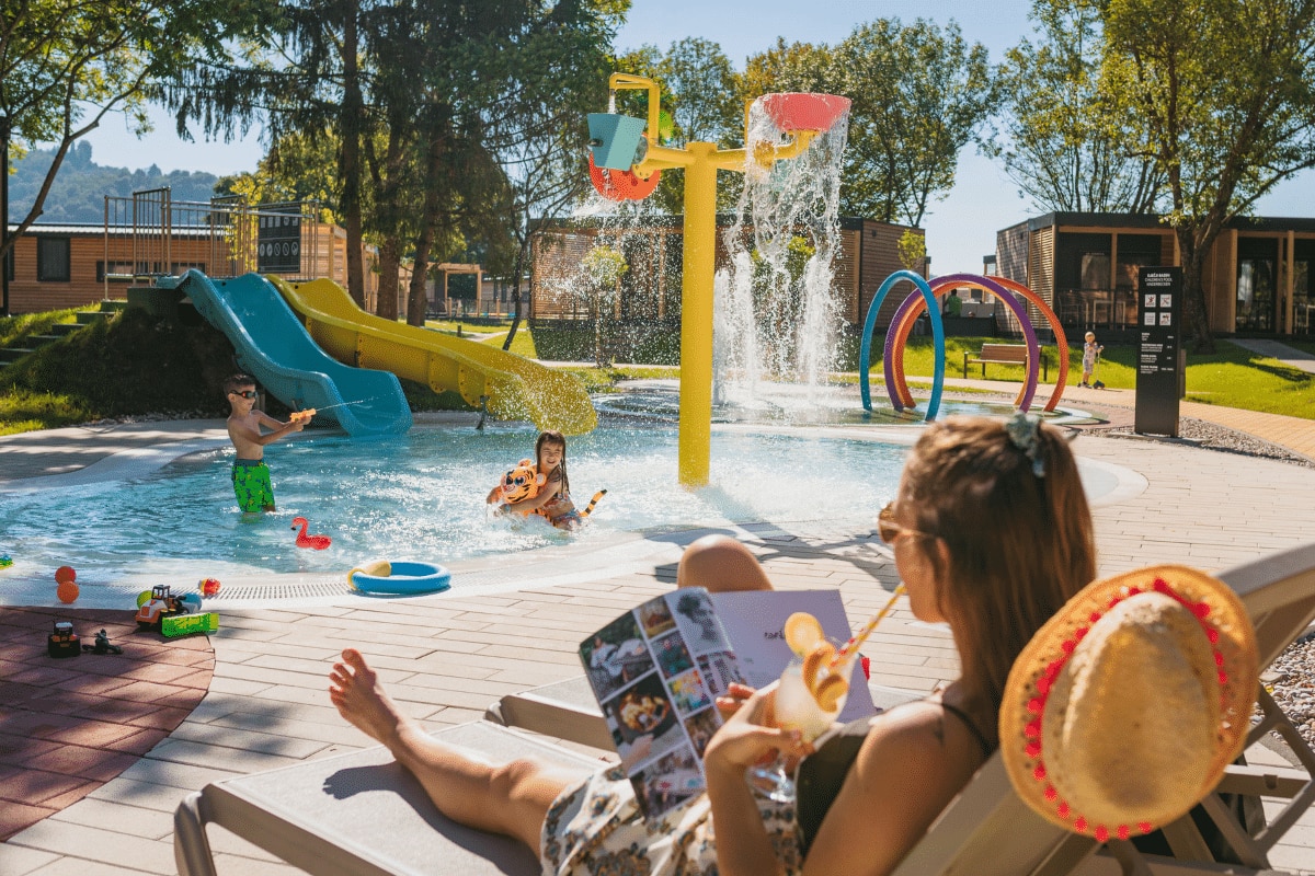 kinderen spelen in zwembad, moeder leest een tijdschrift op een ligbed