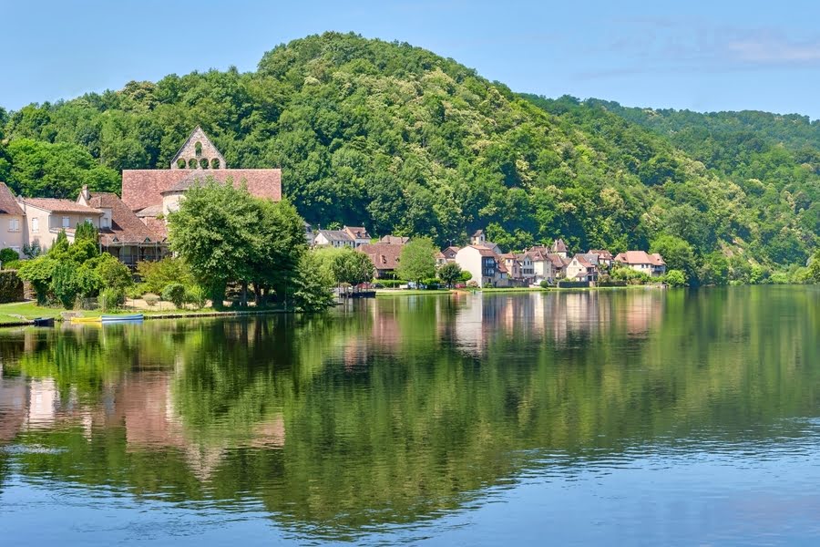 dorp aan oever van een rivier, aan de voet van groene heuvel