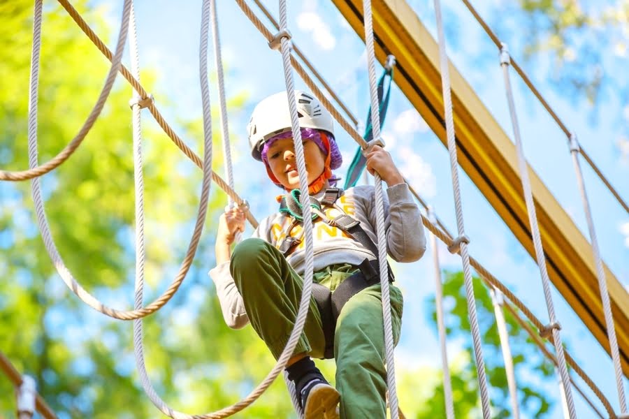 kind met zekering loopt over een touwbrug